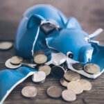 closeup of shattered broken piggy bank with coins on rustic wooden table
