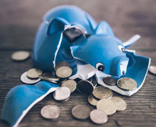 closeup of shattered broken piggy bank with coins on rustic wooden table